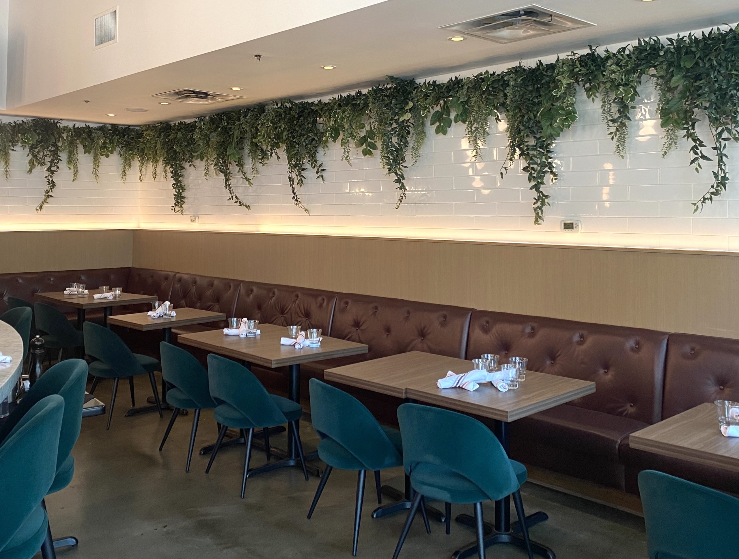 A stylish restaurant interior featuring faux hanging greenery along a white subway tile wall, enhancing the ambiance with lush, cascading artificial plants.