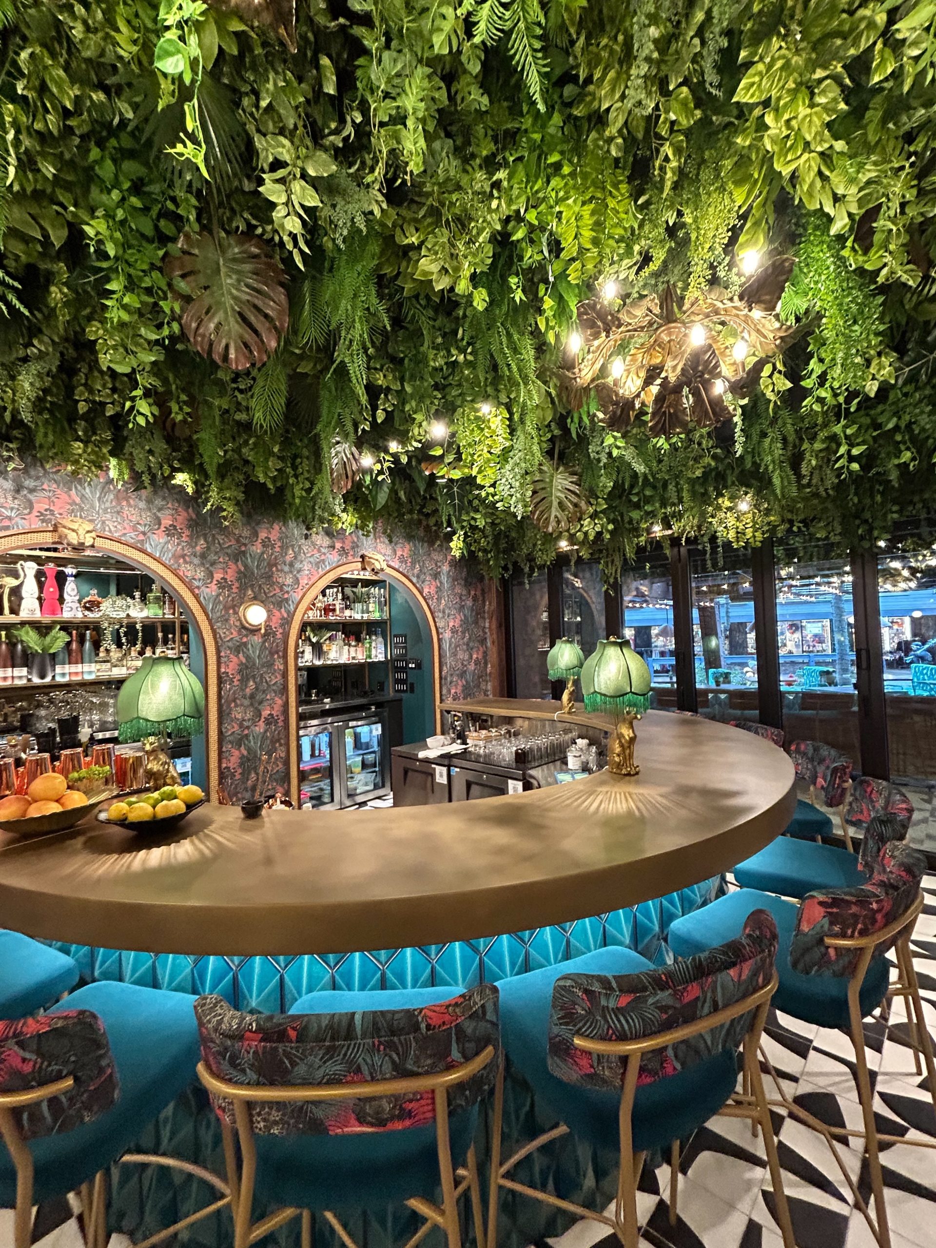 A bar with luxurious decor, featuring artificial ceiling greenery with ferns, vines, and tropical leaves for a lush jungle-inspired ambiance.