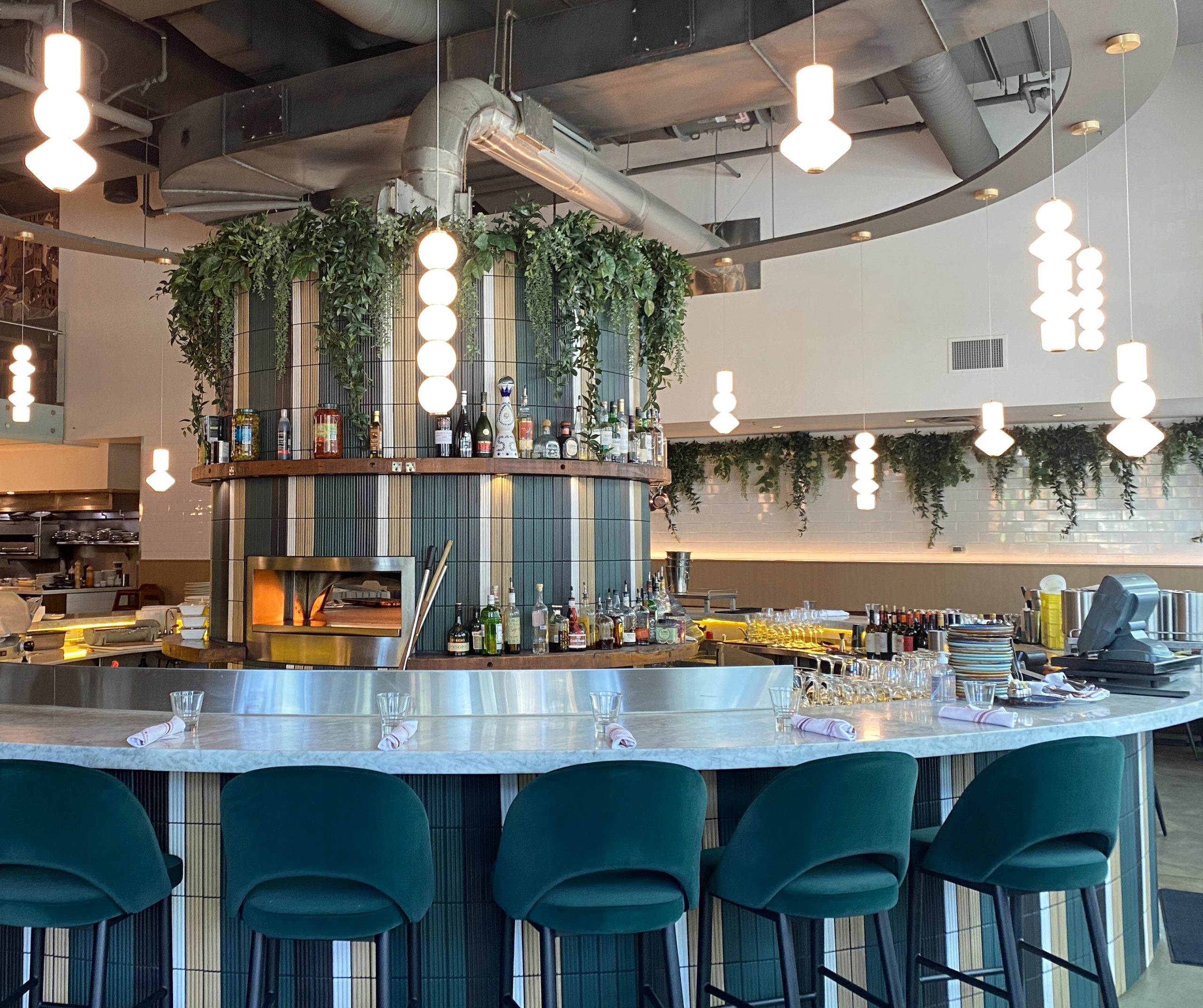 A stylish restaurant bar featuring lush artificial plant installations draping over the counter and along the walls, enhancing the space with a biophilic touch.