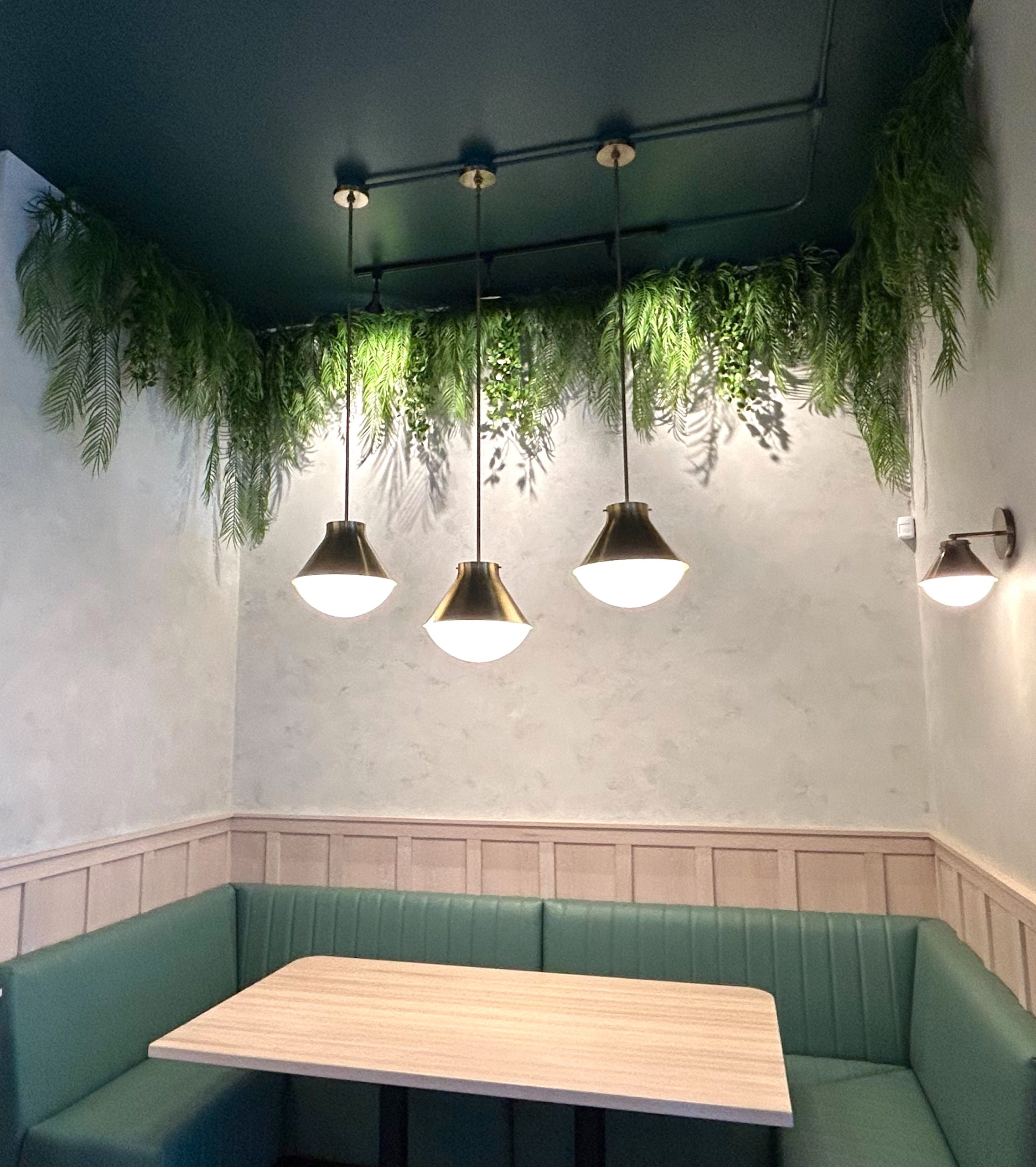 Artificial trailing greenery installation above a cozy booth seating area at Beach House White Rock, featuring modern pendant lighting and a serene dining atmosphere.