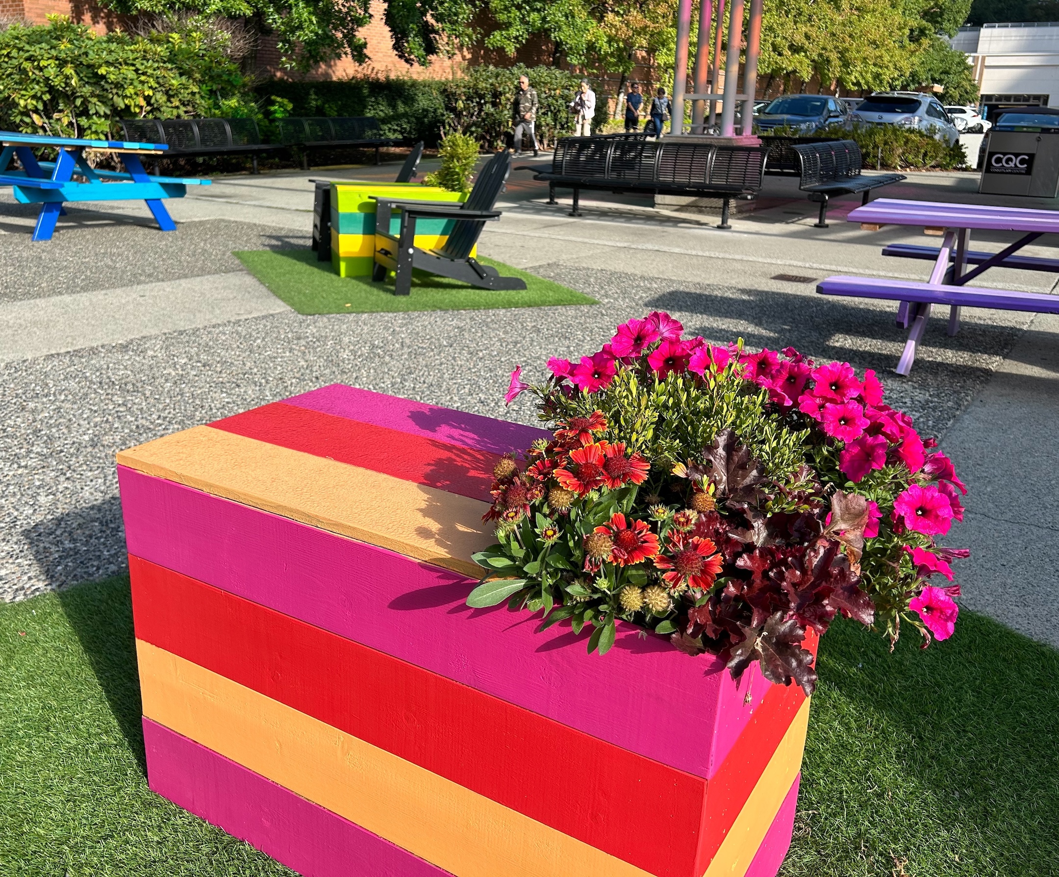 Outdoor patio activation at Coquitlam Shopping Centre featuring colorful striped planters with vibrant flowers and modern seating.