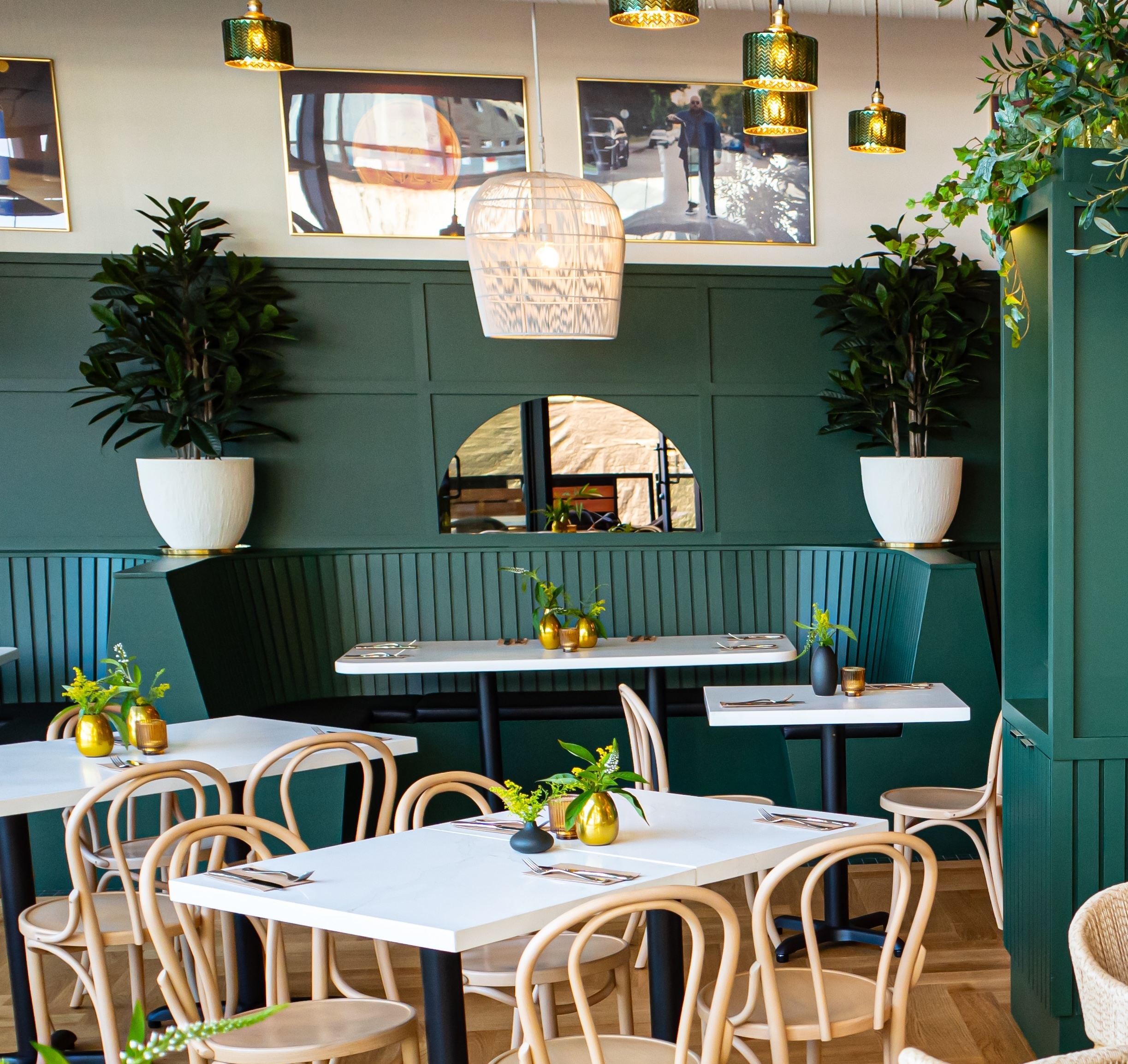 Faux potted plants in white planters complement a stylish restaurant interior with green paneling and natural wood accents, adding warmth and biophilic design.