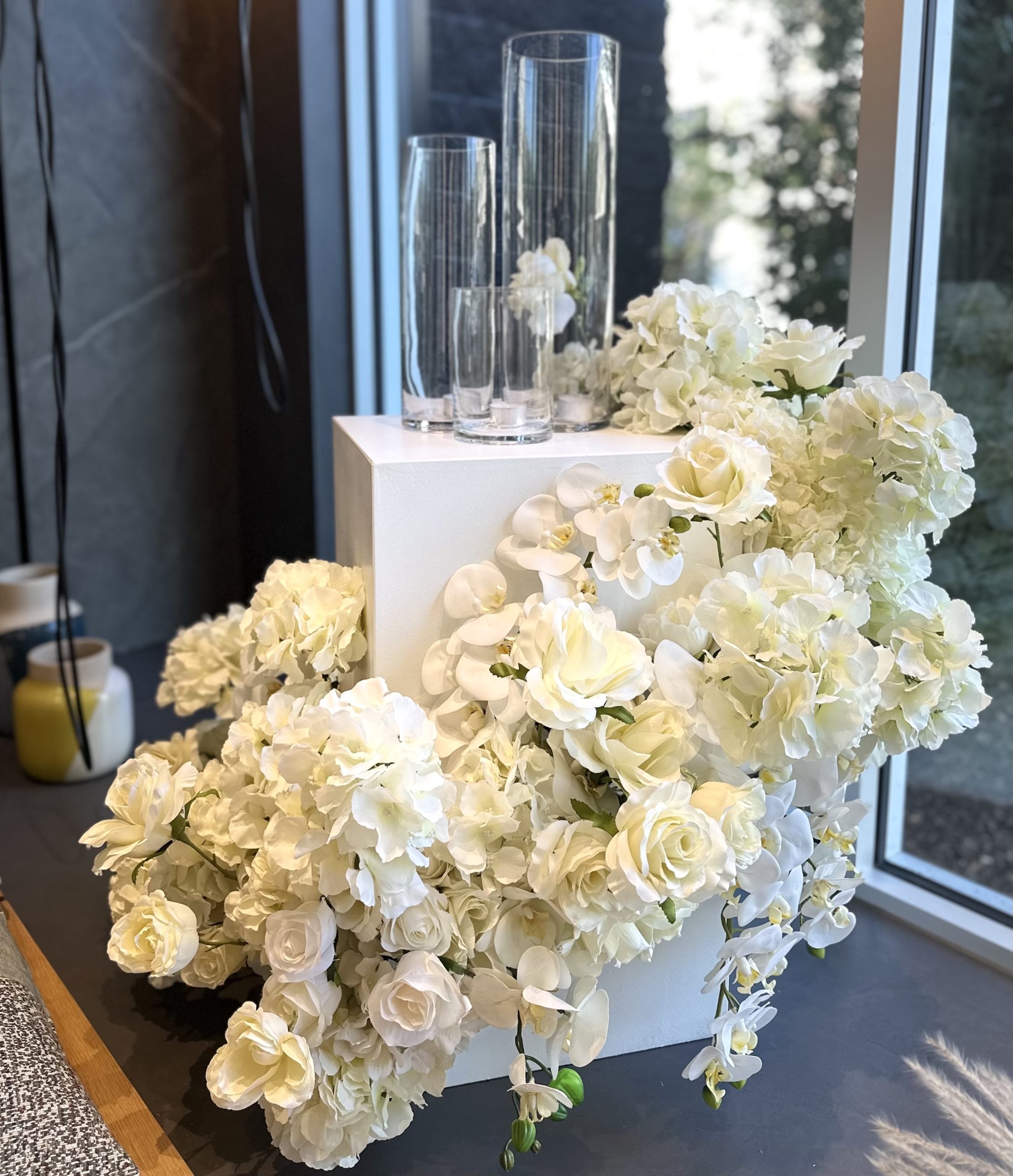 Elegant faux floral arrangement with cascading white roses, orchids, and hydrangeas in a front window of an event space.