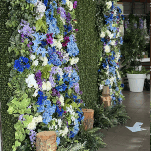 Artificial blue wildflower backdrop with purple, white, and green faux floral accents.