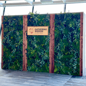Moss wall backdrop rental Vancouver with preserved greenery, vertical wood beams, and event signage for Gathering Wisdom.