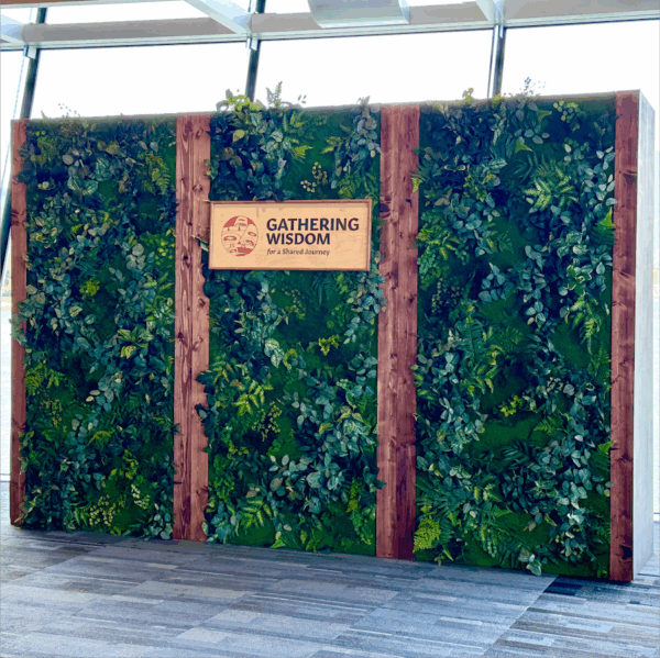 Moss wall backdrop rental Vancouver with preserved greenery, vertical wood beams, and event signage for Gathering Wisdom.