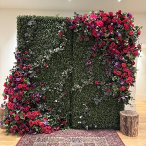 Secret garden-inspired floral wall with red and purple flowers on artificial boxwood greenery, styled by Greenscape Design.
