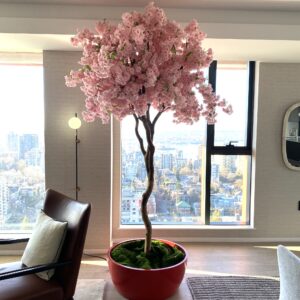Artificial cerise cherry blossom tree in a modern red bowl planter, styled in a contemporary high-rise living space with city views.