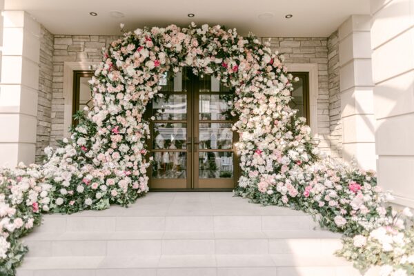 Custom wedding floral arch with cascading blush, ivory, and white artificial flowers framing a grand entrance.