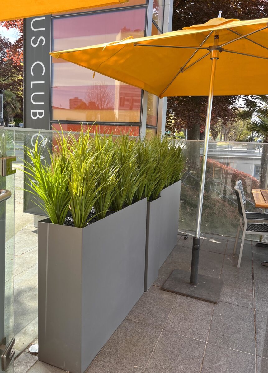 Outdoor restaurant patio featuring tall faux grasses in sleek metal planters for stylish, low-maintenance greenery.