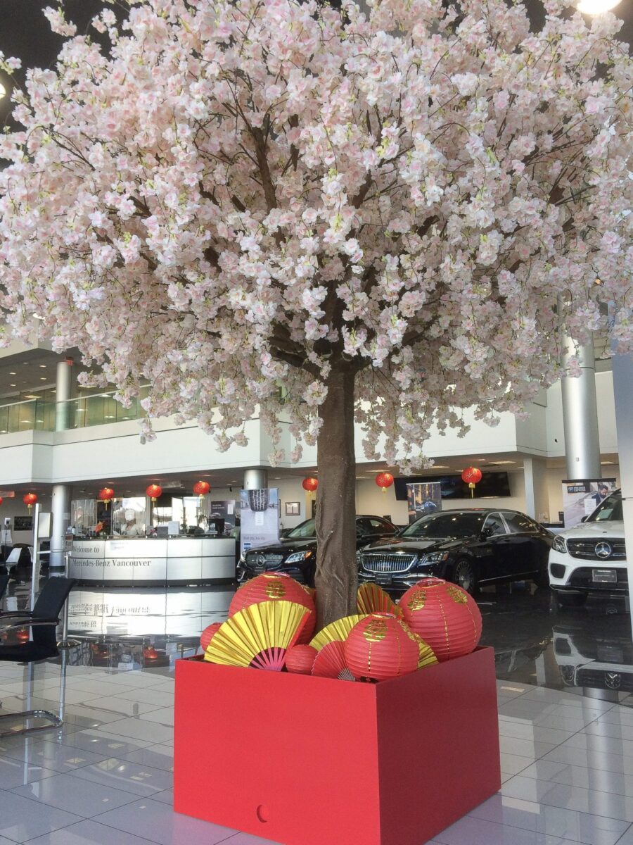 Indoor cherry blossom tree display with red Lunar New Year lanterns and fans in a commercial showroom lobby