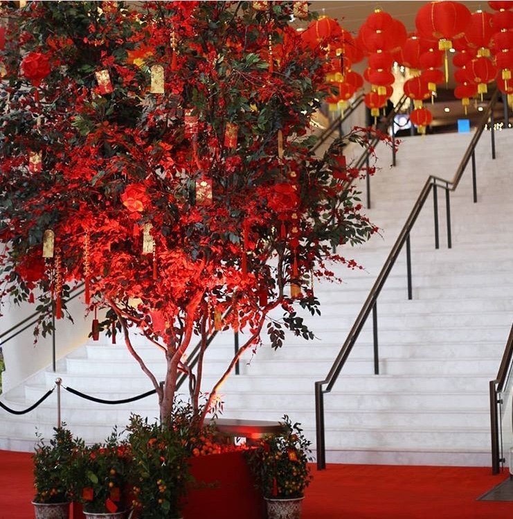 Red-themed Lunar New Year tree installation with hanging lanterns near the staircase in a commercial space