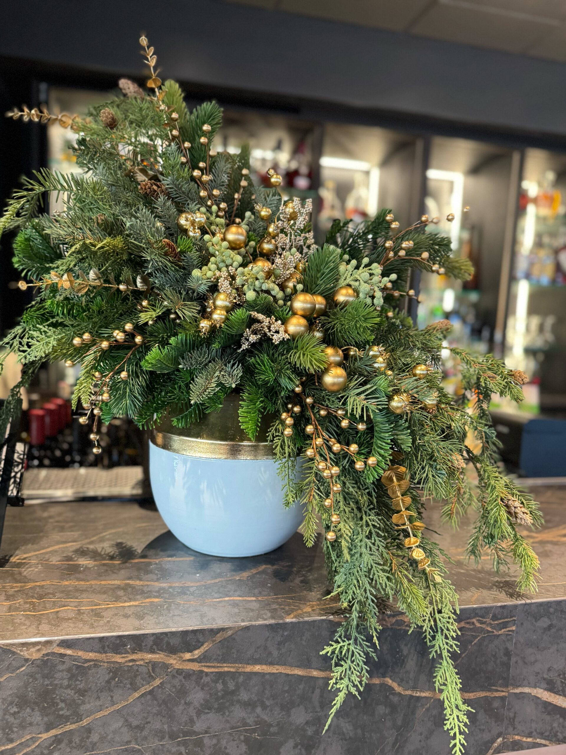Holiday greenery arrangement with gold accents in planter on a counter