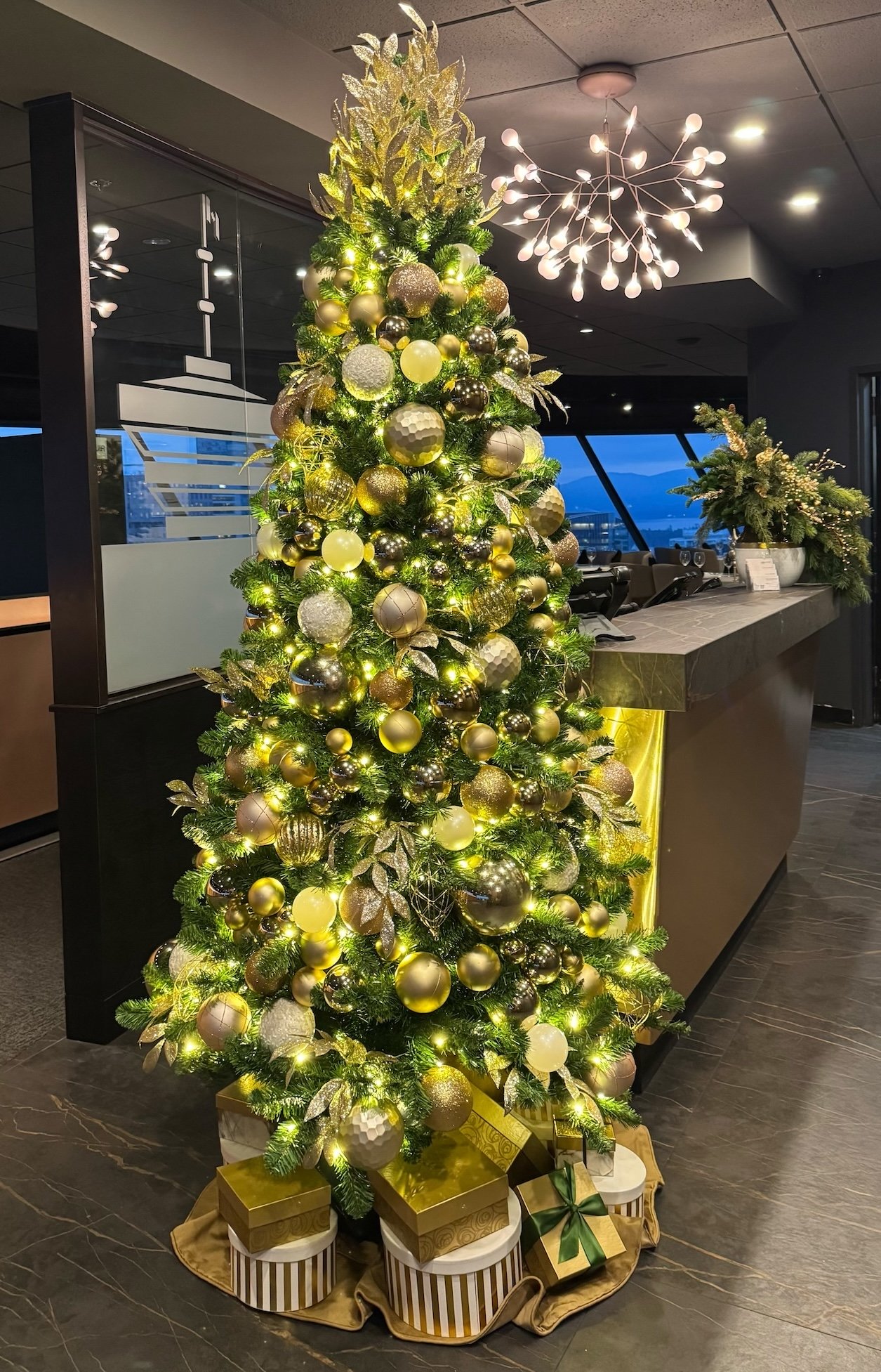 Luxury metallic Christmas tree with gold ornaments beside reception desk