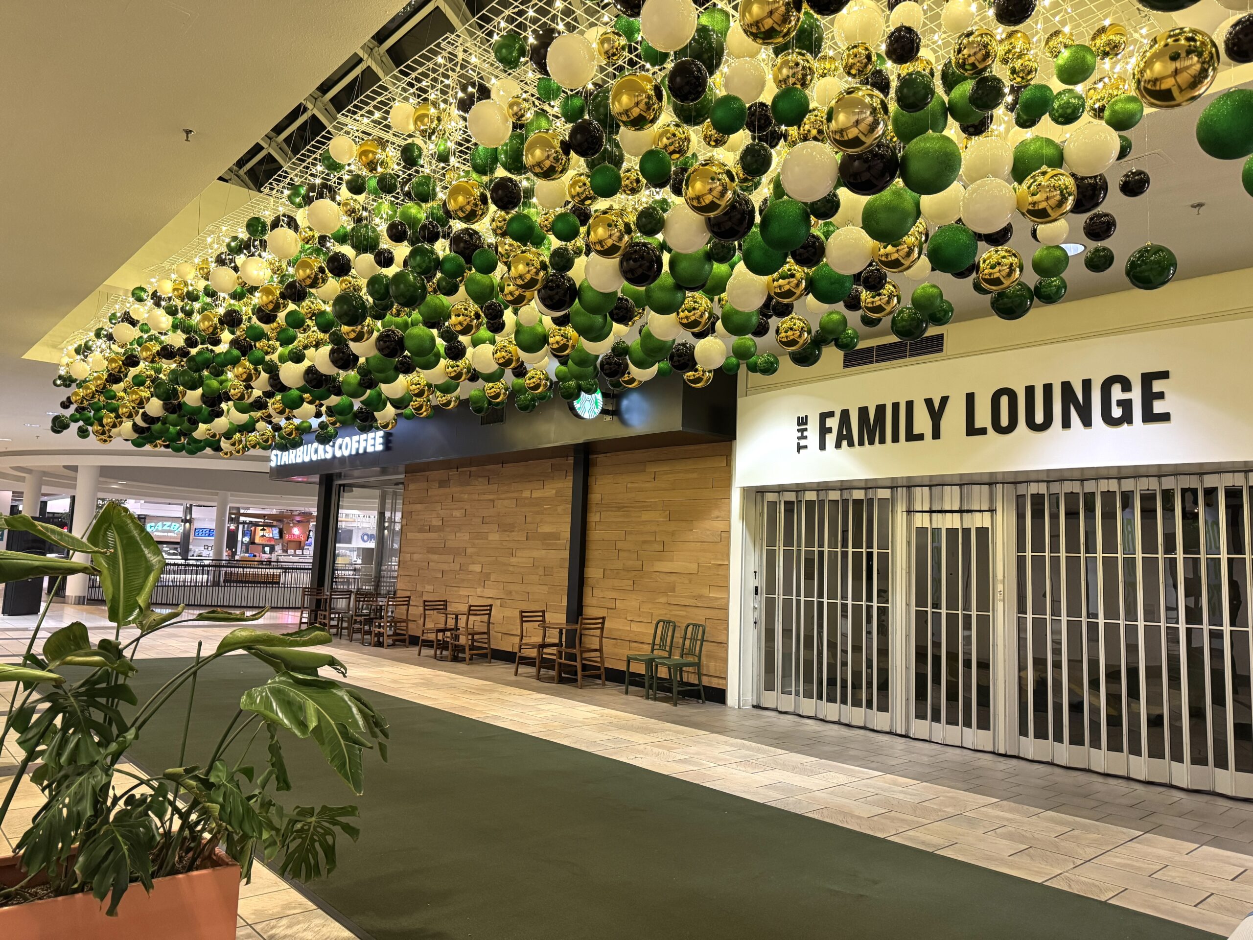 Green, white, black, and gold baubles suspended from ceiling in shopping mall corridor