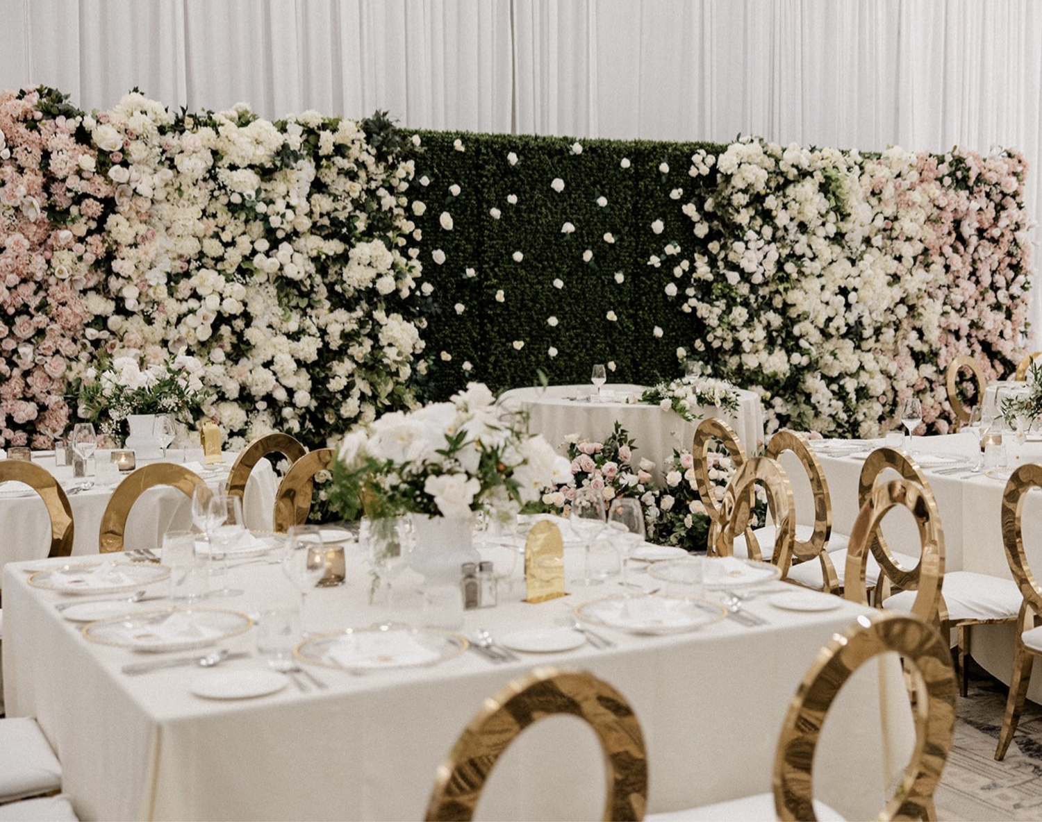 Boxwood floral wall with white and blush flowers behind reception table