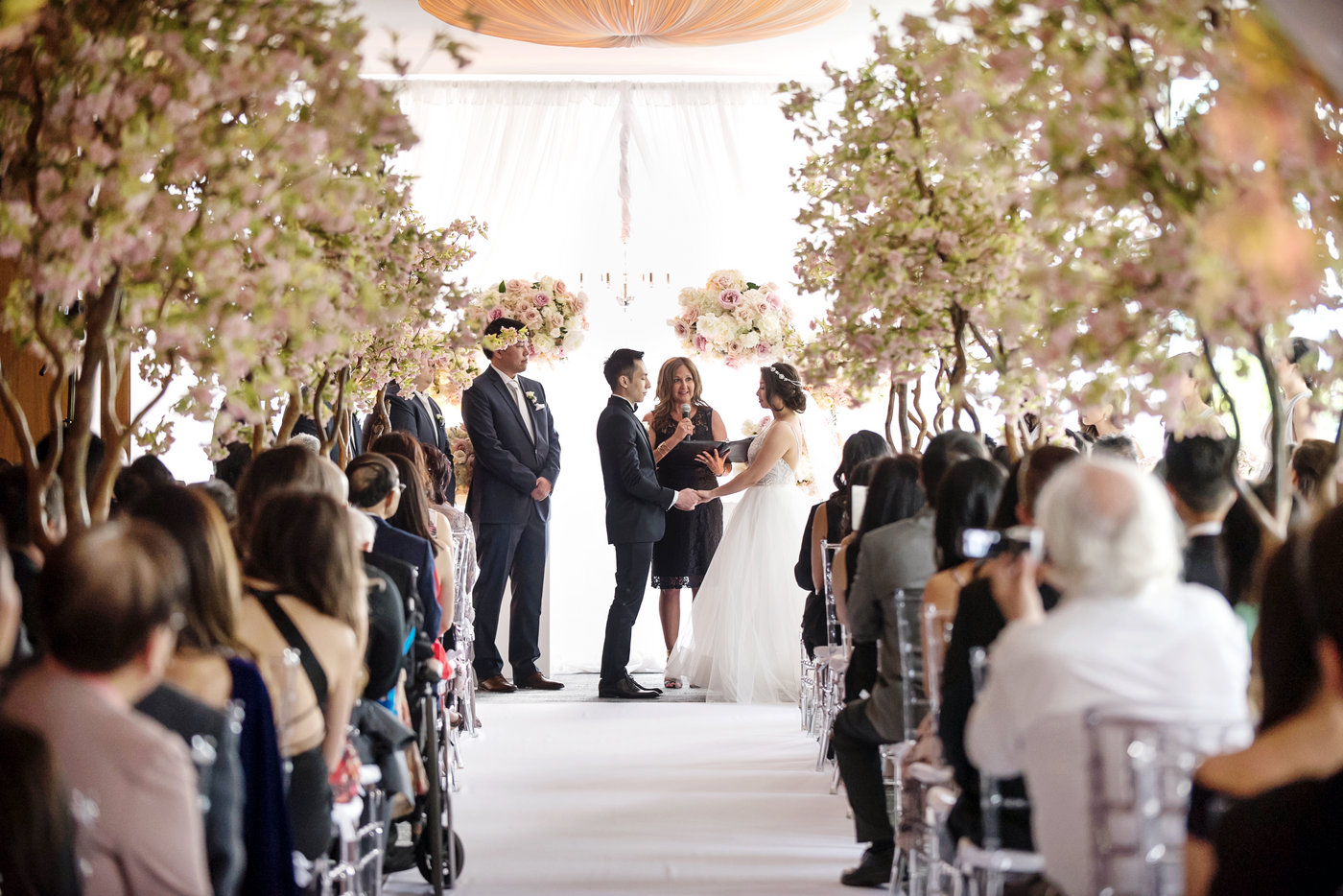 Indoor wedding ceremony aisle lined with cherry blossom trees