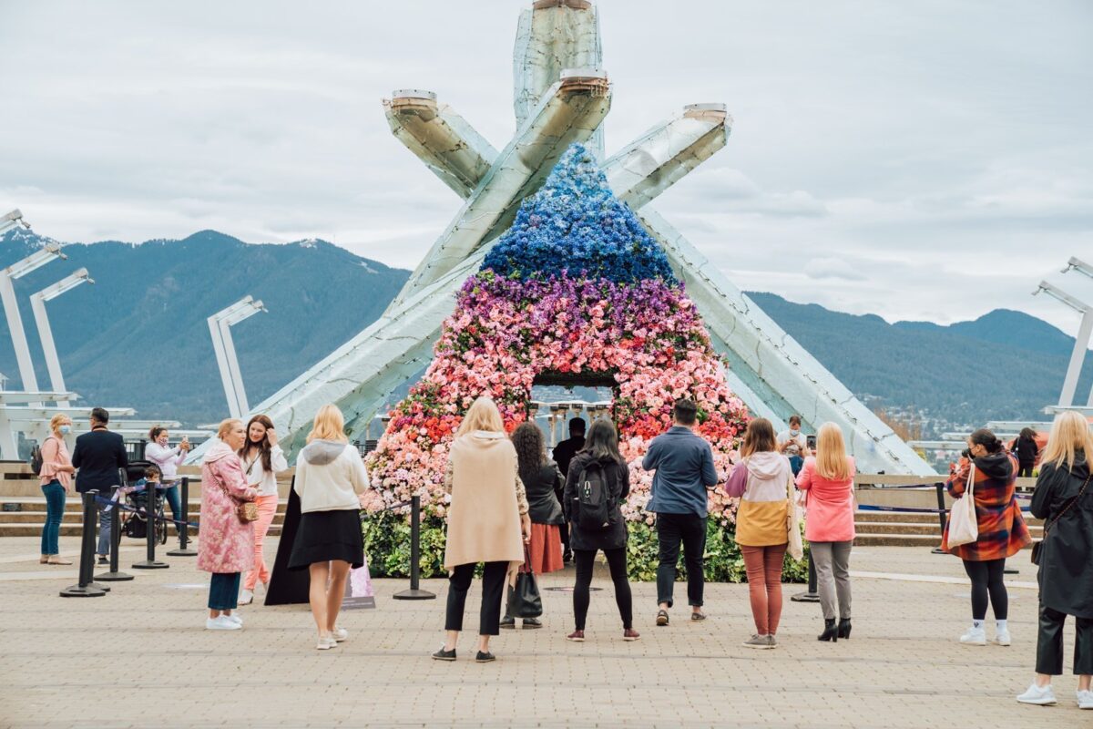 Large floral arch installation at an outdoor public plaza with people gathered