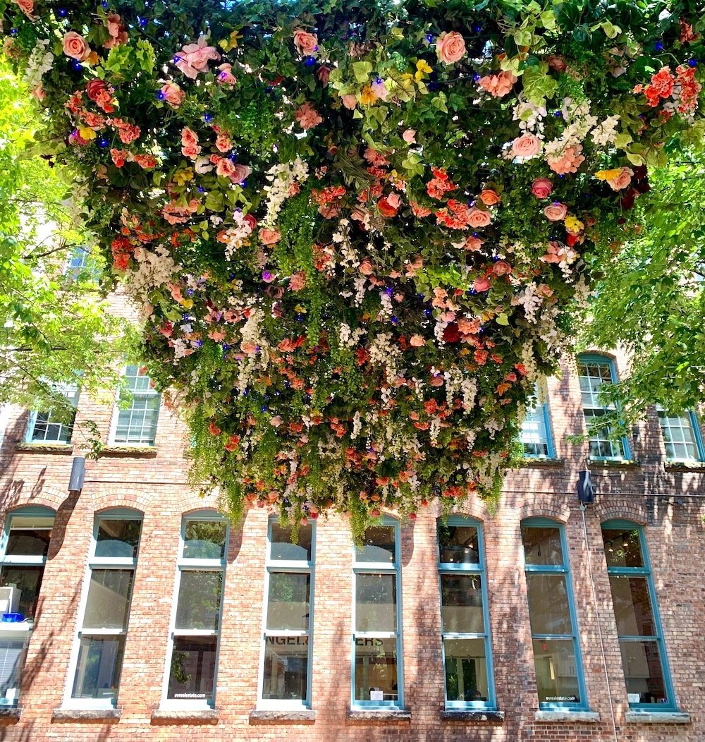 Artificial floral ceiling installation with cascading greenery suspended in front of a brick building
