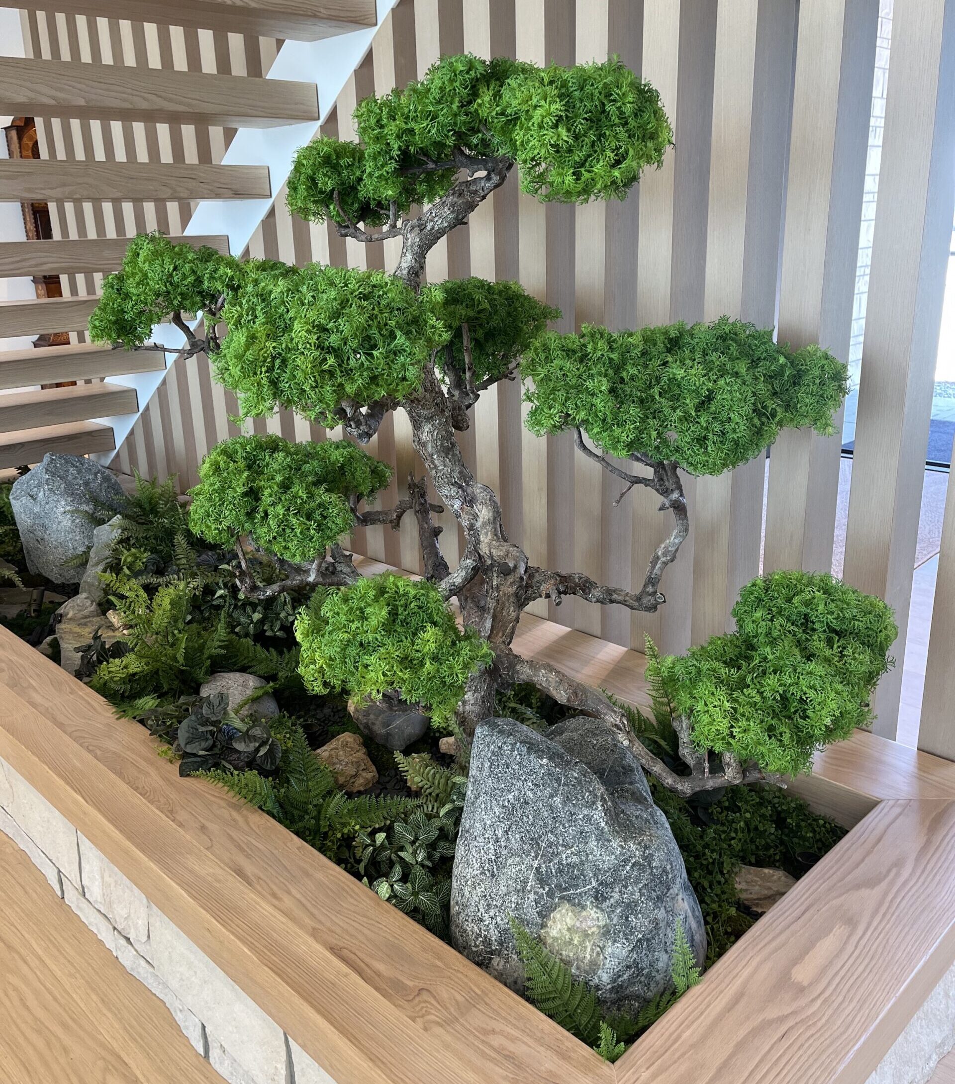 Artificial pine bonsai tree displayed indoors beneath a staircase