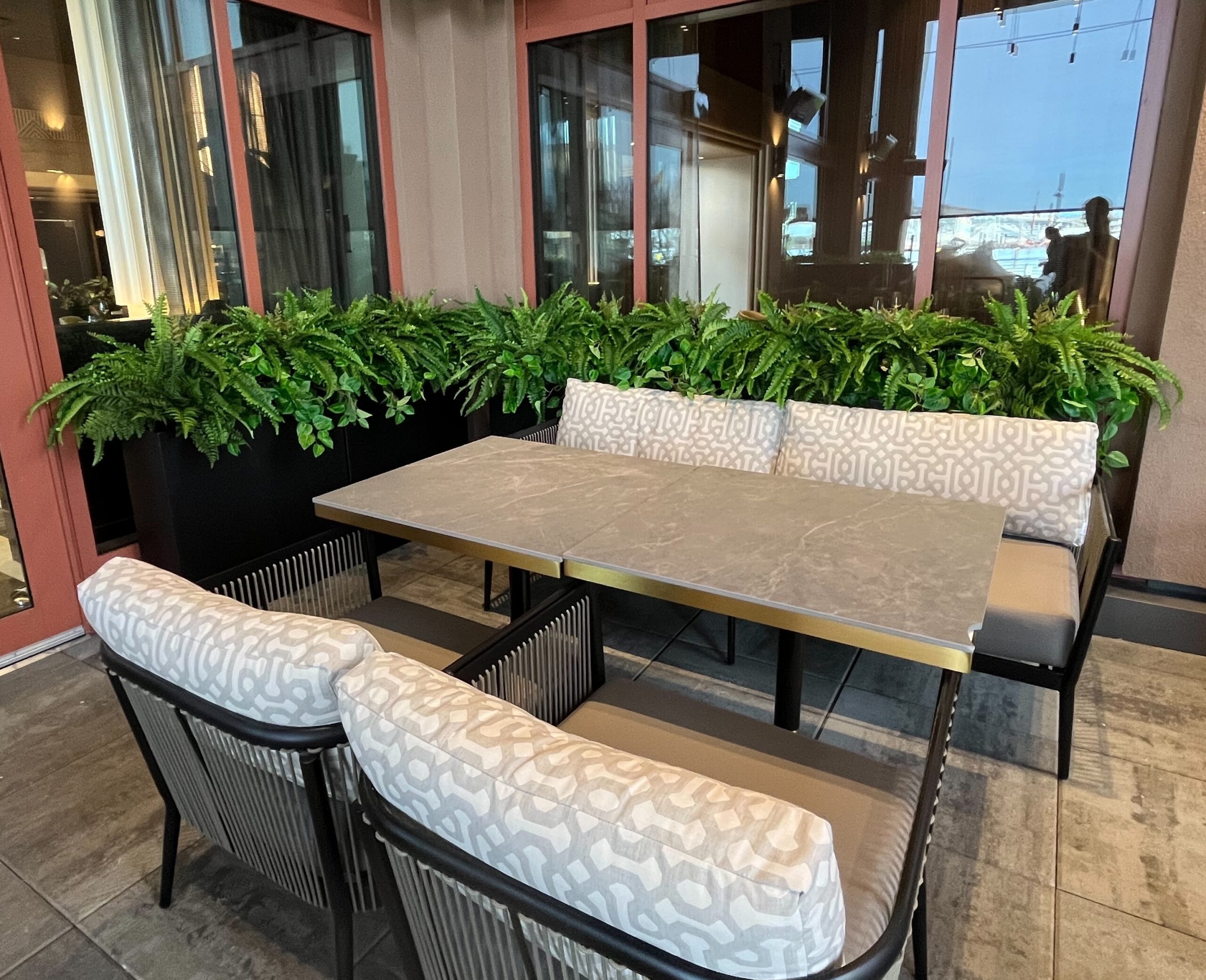 Artificial potted ferns in a long planter behind banquette seating along restaurant windows