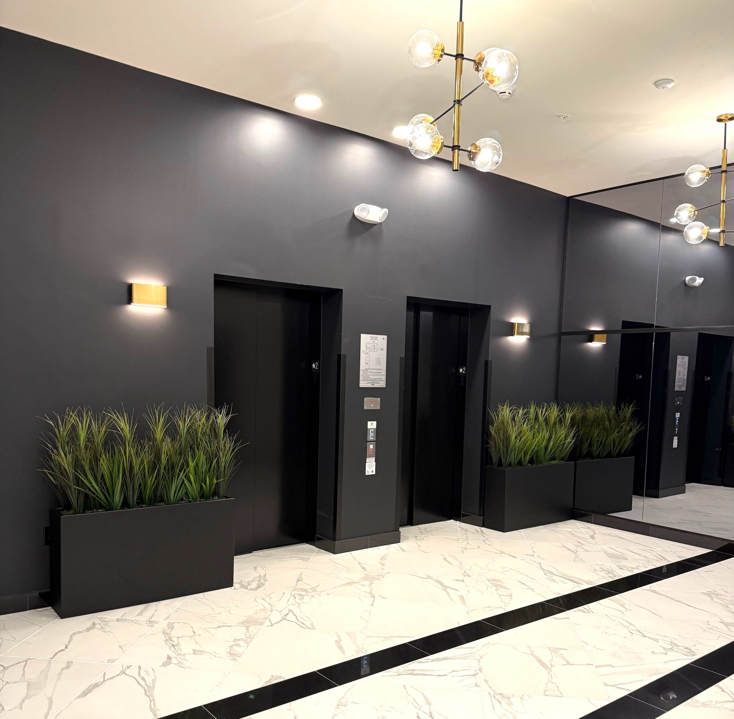 Artificial potted grass in rectangular planters placed near elevator doors in a modern office lobby