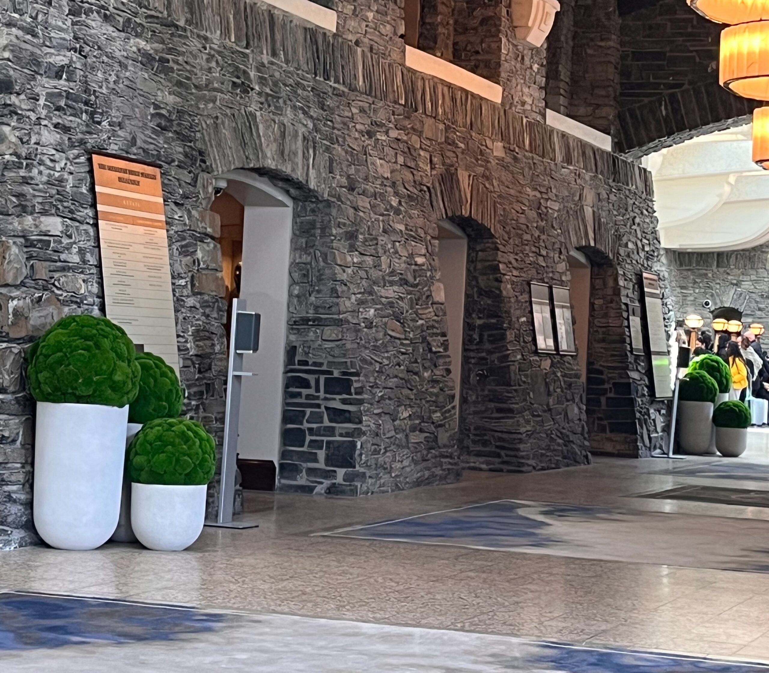 White floor planters with rounded green preserved moss forms placed along a stone wall in a hotel lobby.