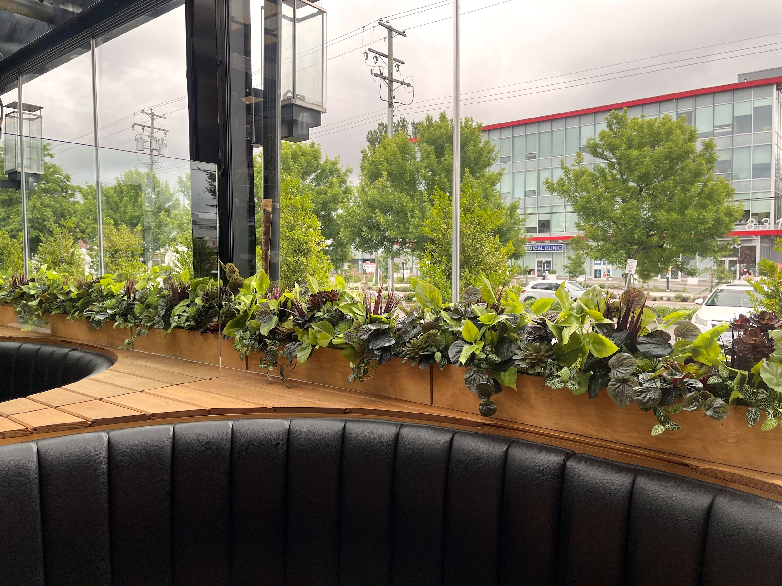 Long wood window planter filled with artificial leafy greenery, succulents and burgundy accent plants behind curved restaurant booth seating.