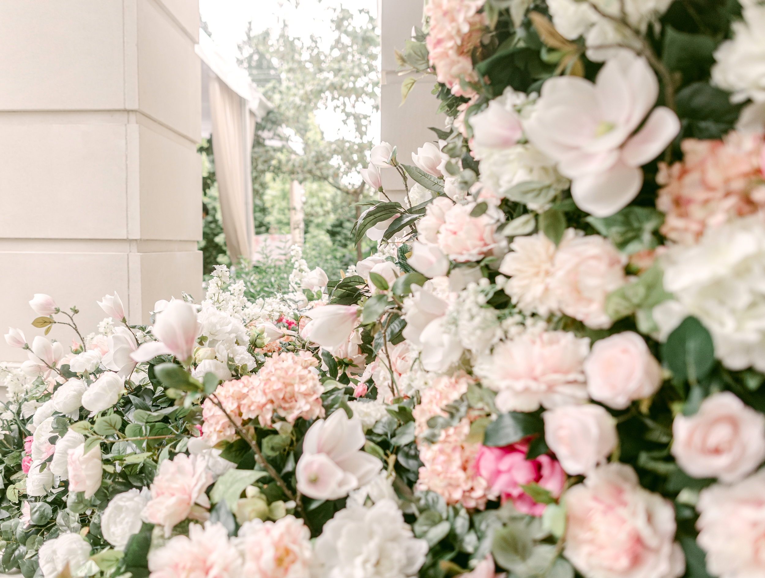 Large pink and white floral arch closeup with magnolia blooms, roses, and hydrangea arranged around an outdoor venue entrance.