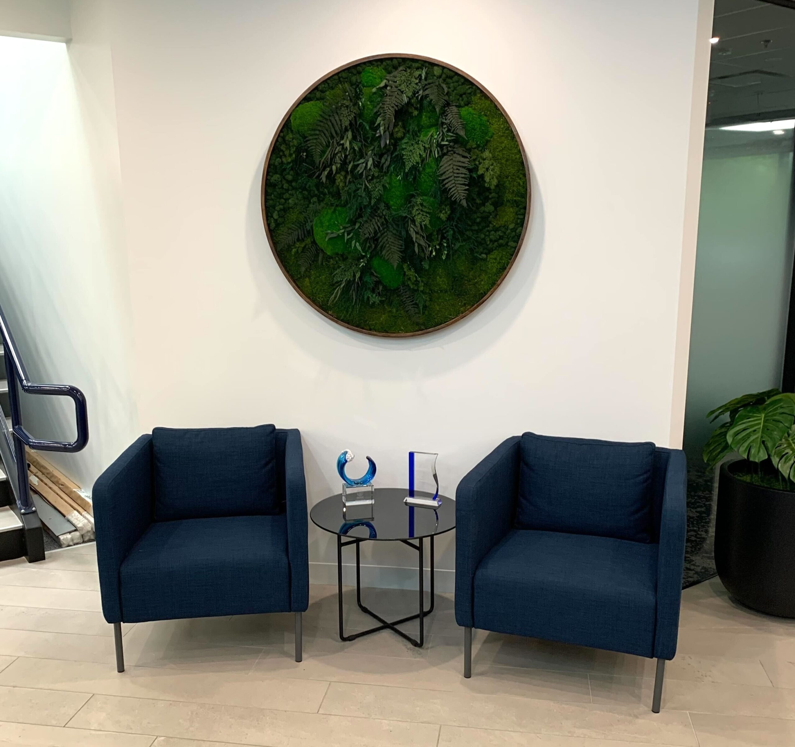 Round framed moss wall art with layered preserved moss and fern foliage mounted on a white office wall.