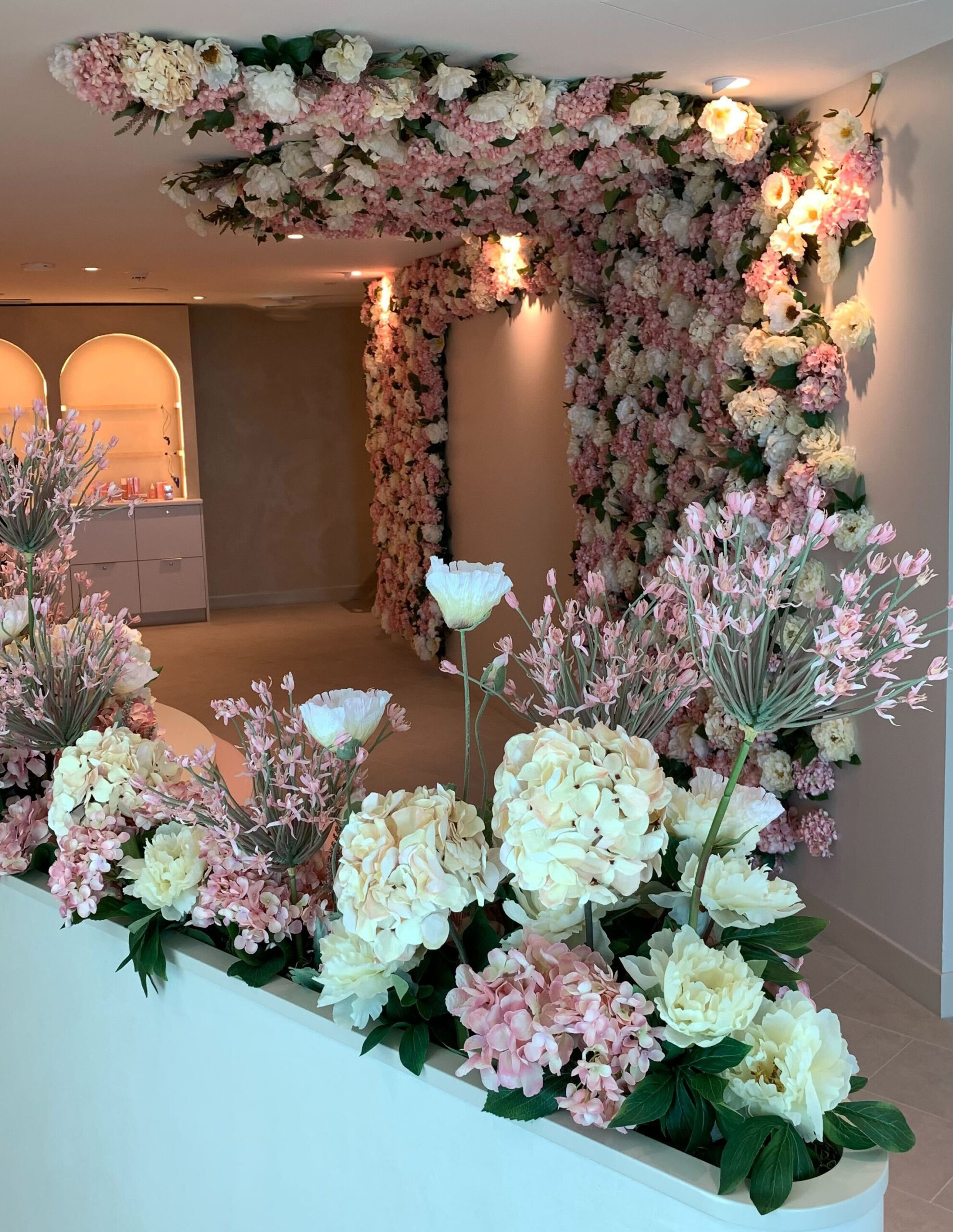Commercial interior with blush and ivory faux floral installations across the ceiling, walls, and planter ledge with layered floral groupings.