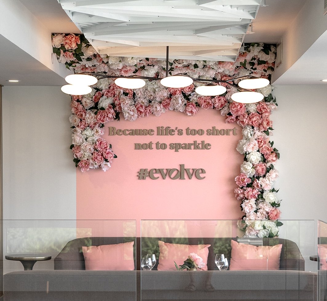 Pink feature wall with white and blush faux floral installation framing the top and right side above commercial lounge seating.