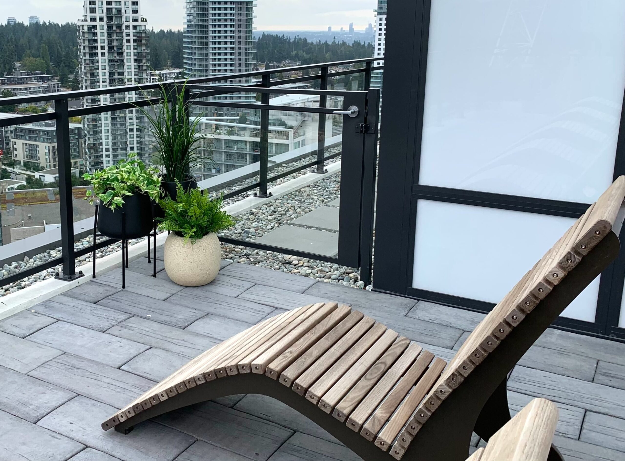 Rooftop condo patio with potted artificial grass, faux trailing greenery and fern planter beside a privacy screen and lounge chairs.