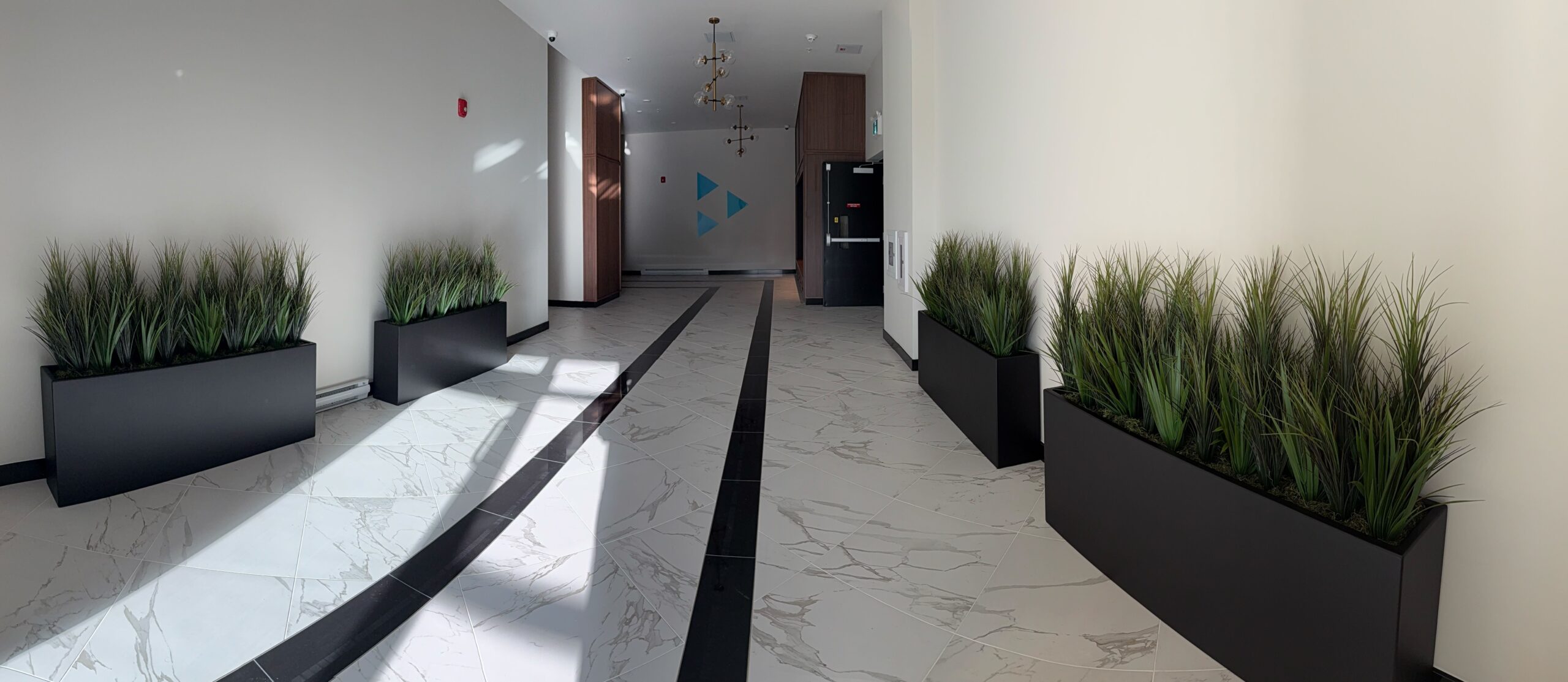 Faux potted grass arranged in long planters along a bright lobby corridor