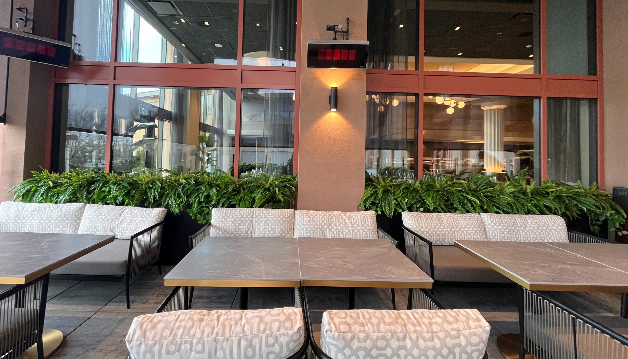Faux potted ferns in a planter behind banquette seating along restaurant windows in a dining area