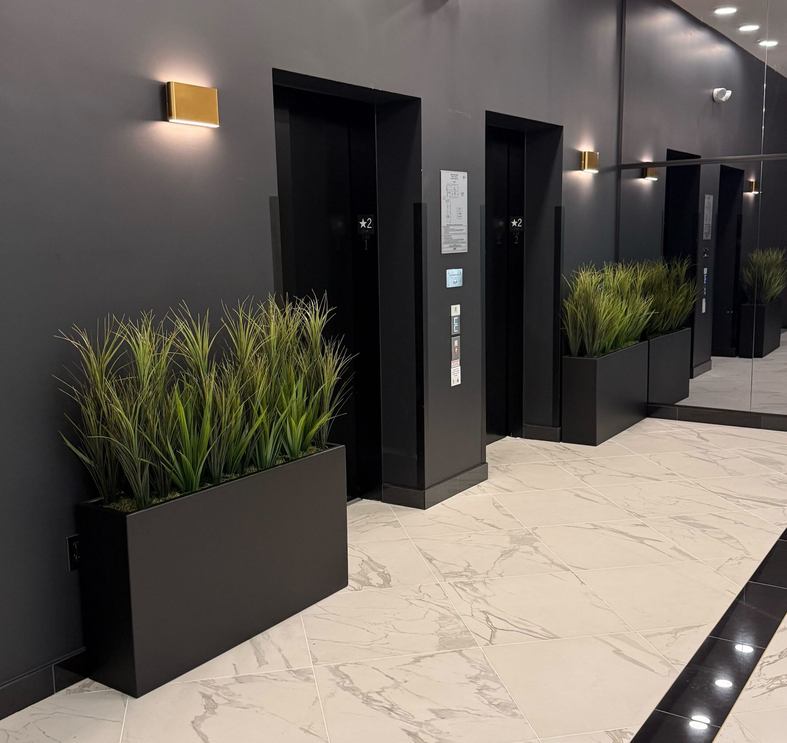 Faux potted grass in planters positioned beside elevator doors in a office lobby setting