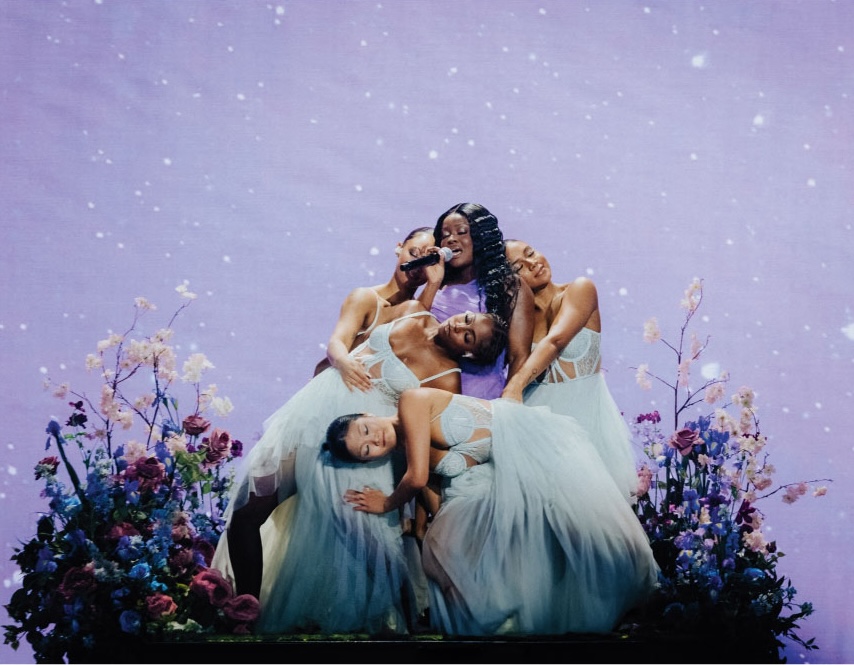 Floral meadow stage with performers surrounded by flowers during music performance.