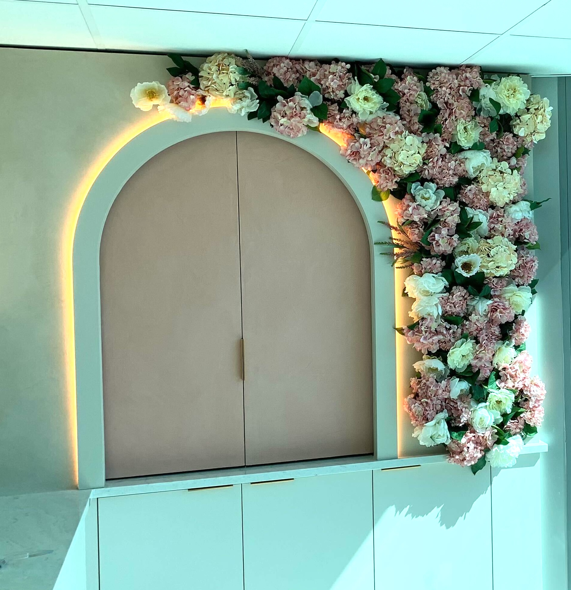 Arched wall niche with integrated blush and ivory faux floral installation cascading across the top and right side in a commercial interior.