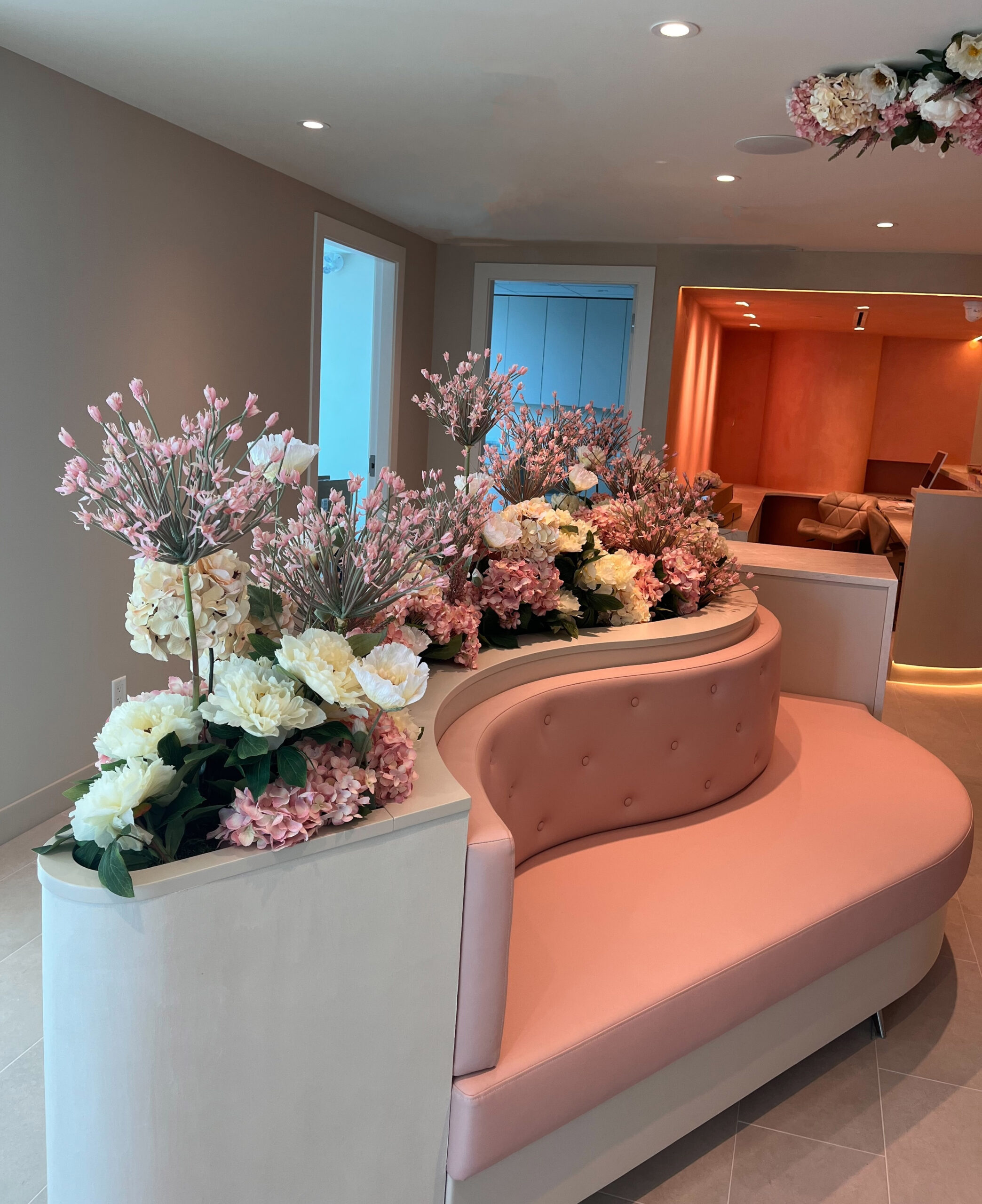 Curved pink commercial bench with faux pink and white floral arrangements built into the back and side planters in a modern interior.
