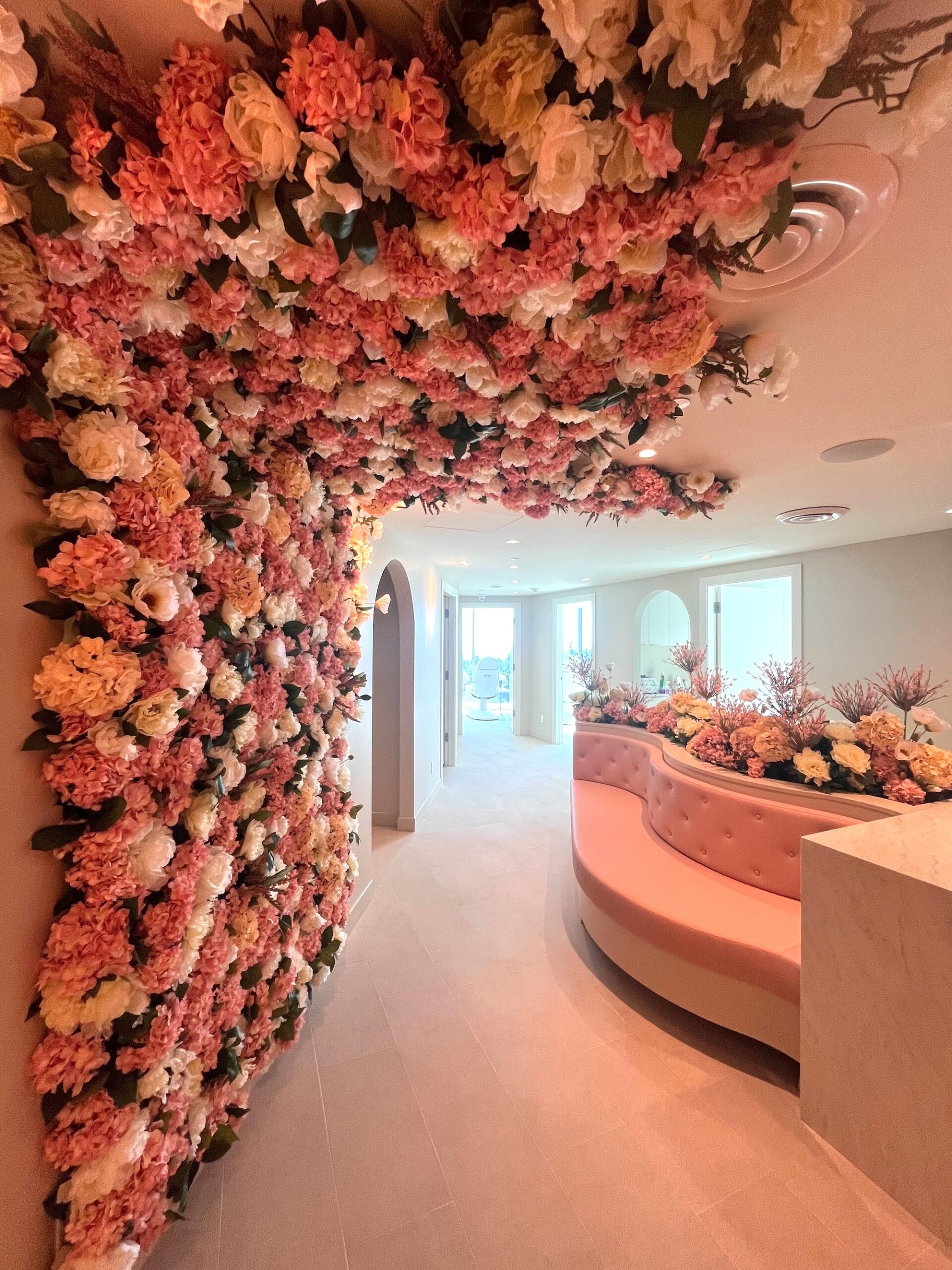 Commercial interior with blush and ivory faux floral installation covering the ceiling and wall beside a curved pink built-in bench.