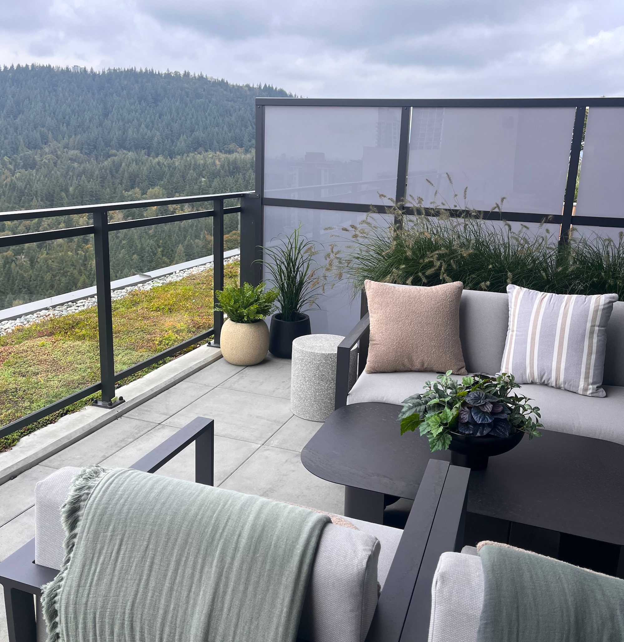 Outdoor balcony with potted artificial grasses and a mixed faux foliage planter beside a privacy screen.