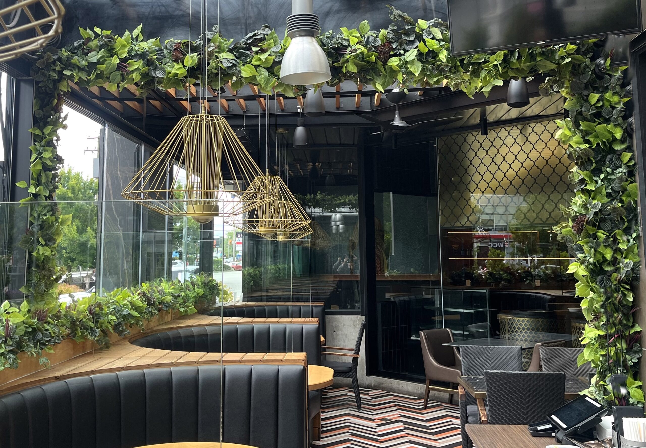 Commercial dining space with faux greenery installed along overhead beams, vertical columns, and planter ledges around booth seating.