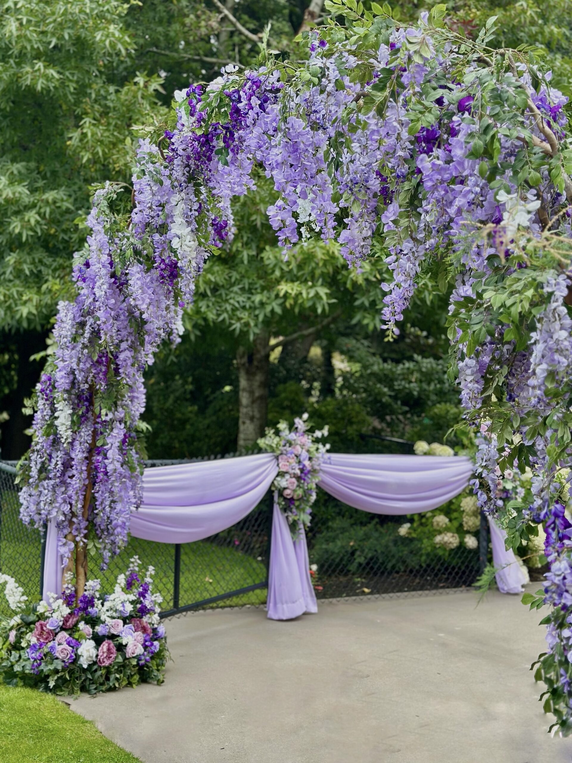 Outdoor entry arch covered in cascading purple wisteria flowers