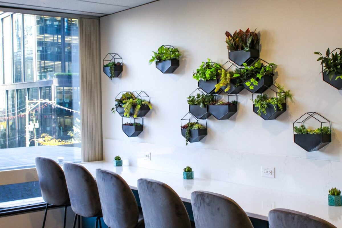 Geometric wall-mounted black planters filled with artificial greenery arranged along the wall of a modern office boardroom