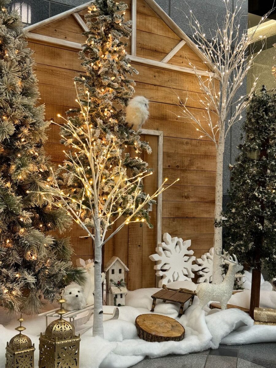A winter-themed holiday display in front of a wooden cabin backdrop