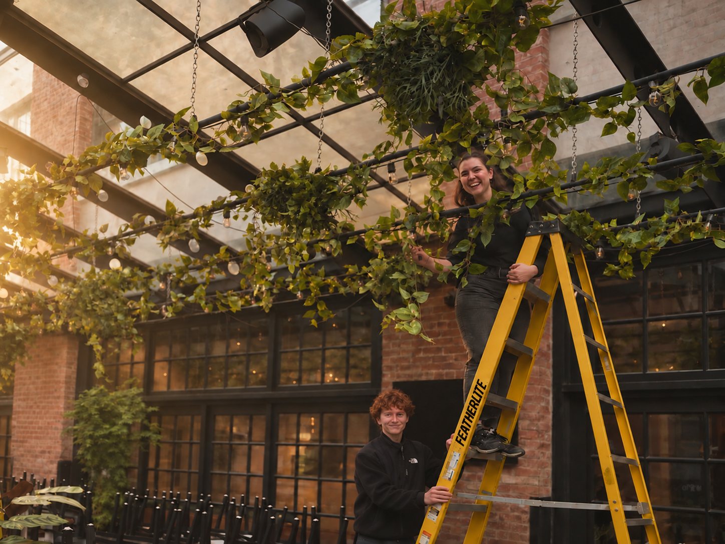 Greenscape installers positioning a large artificial tree in a bright atrium lobby.