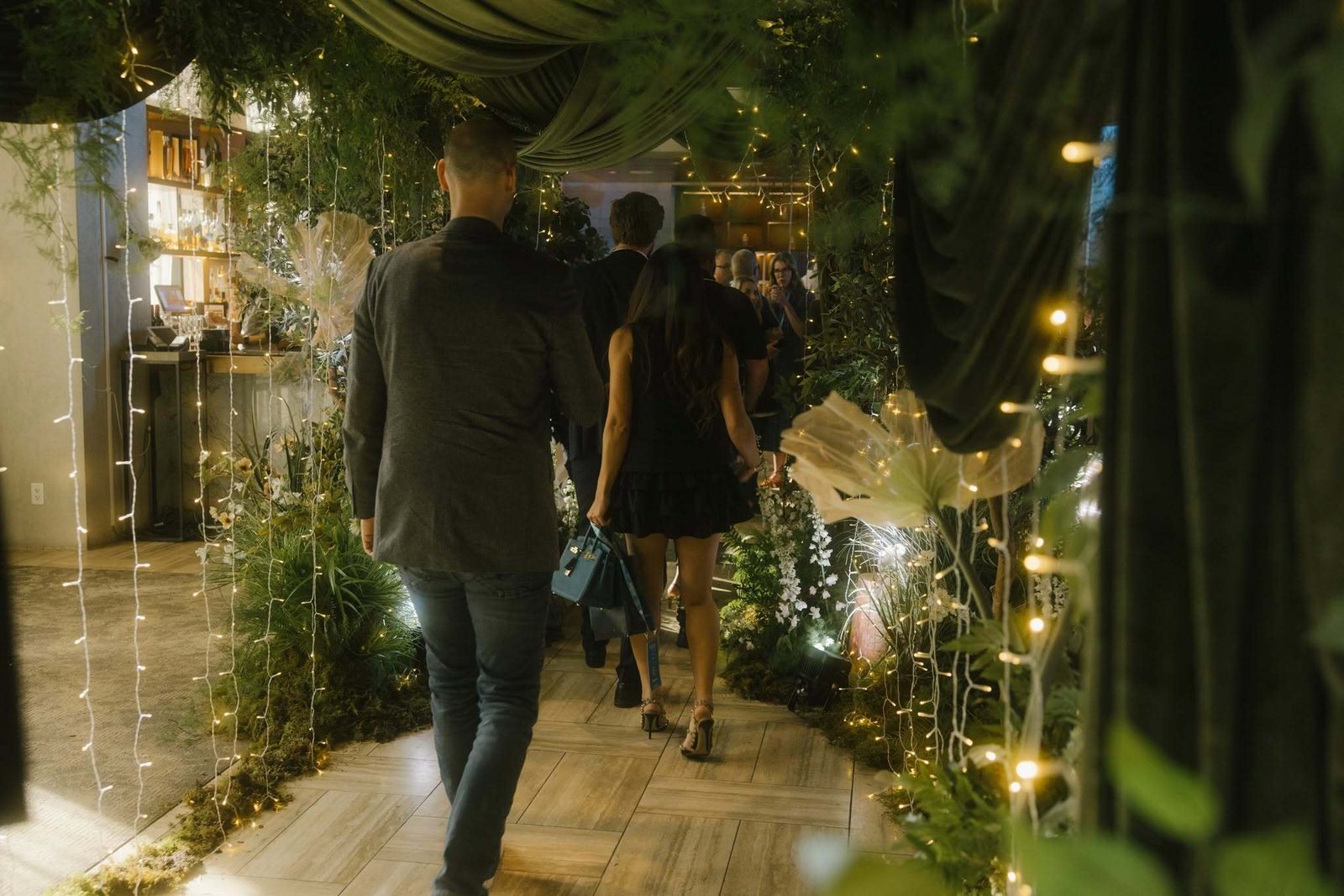 Guests walking through a greenery-lined event entrance with string lights.